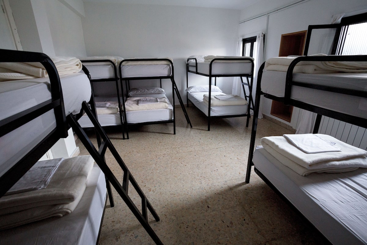 A dormitory room with bunk beds, a window, and a door.