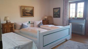 A bedroom with a bed, two nightstands, a window with curtains, a radiator, and two paintings on the wall.