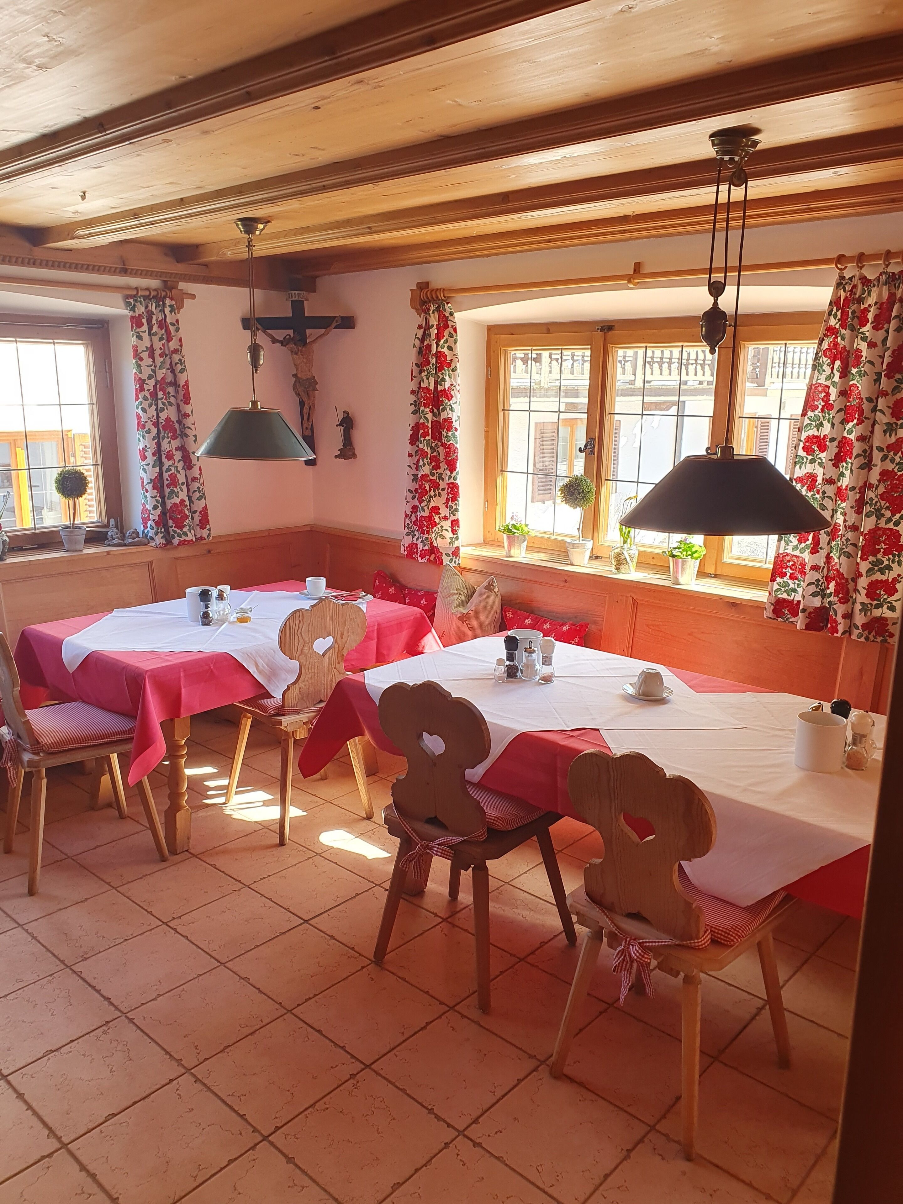 Ein Essbereich mit Holztischen und -stühlen, weißen Tischdecken und roten Vorhängen.