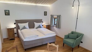 Un dormitorio ordenado con cama, mesitas de noche, una silla, una mesa redonda de madera y una lámpara en el techo.