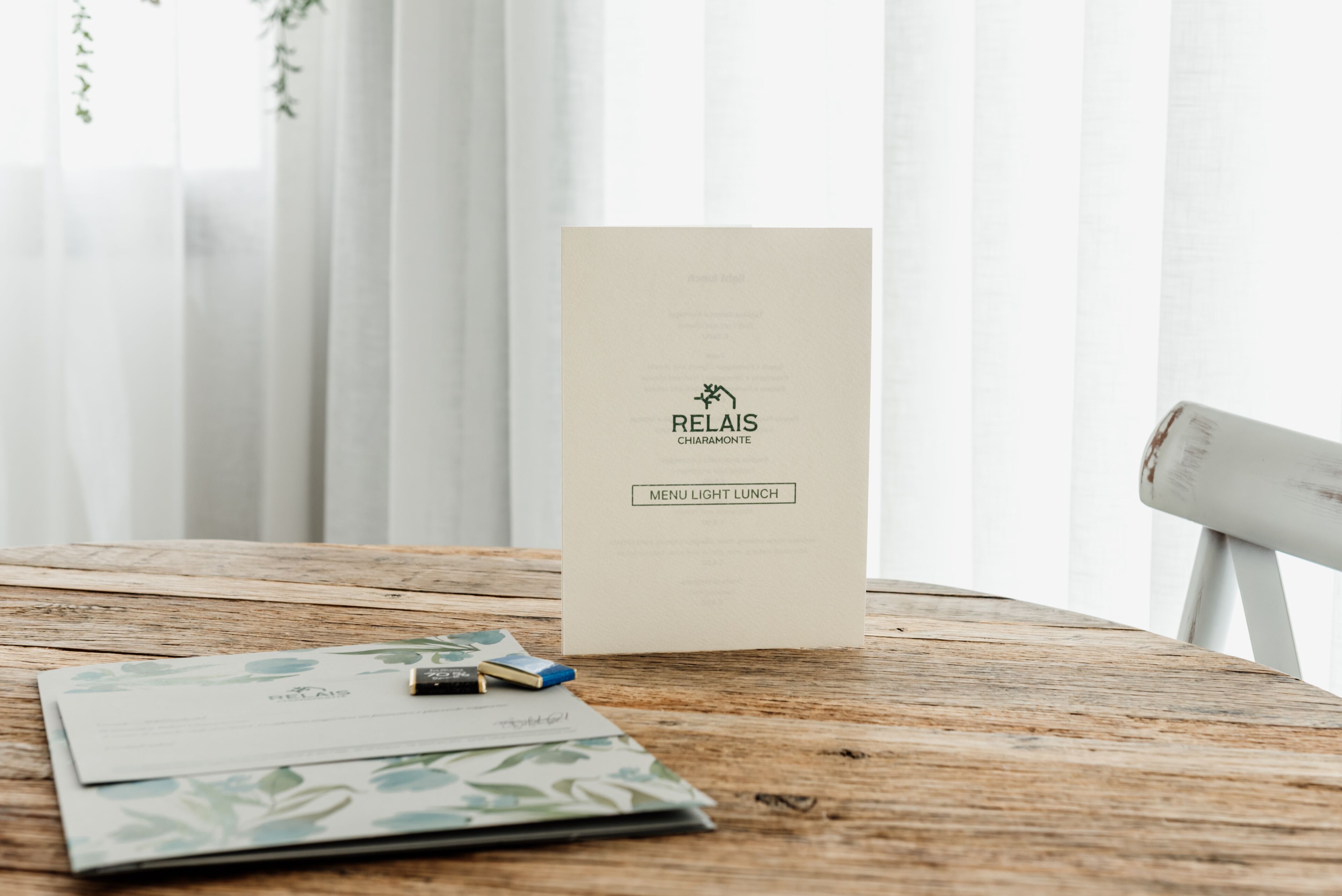 A wooden table with a menu card labeled "RELAIS CHIAMONTE MENU LIGHT LUNCH" and some documents.