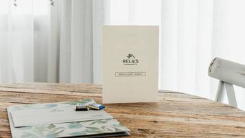 Una mesa de madera con una tarjeta de menú que dice "RELAIS CHIAMONTE MENU LIGHT LUNCH" y algunos documentos.