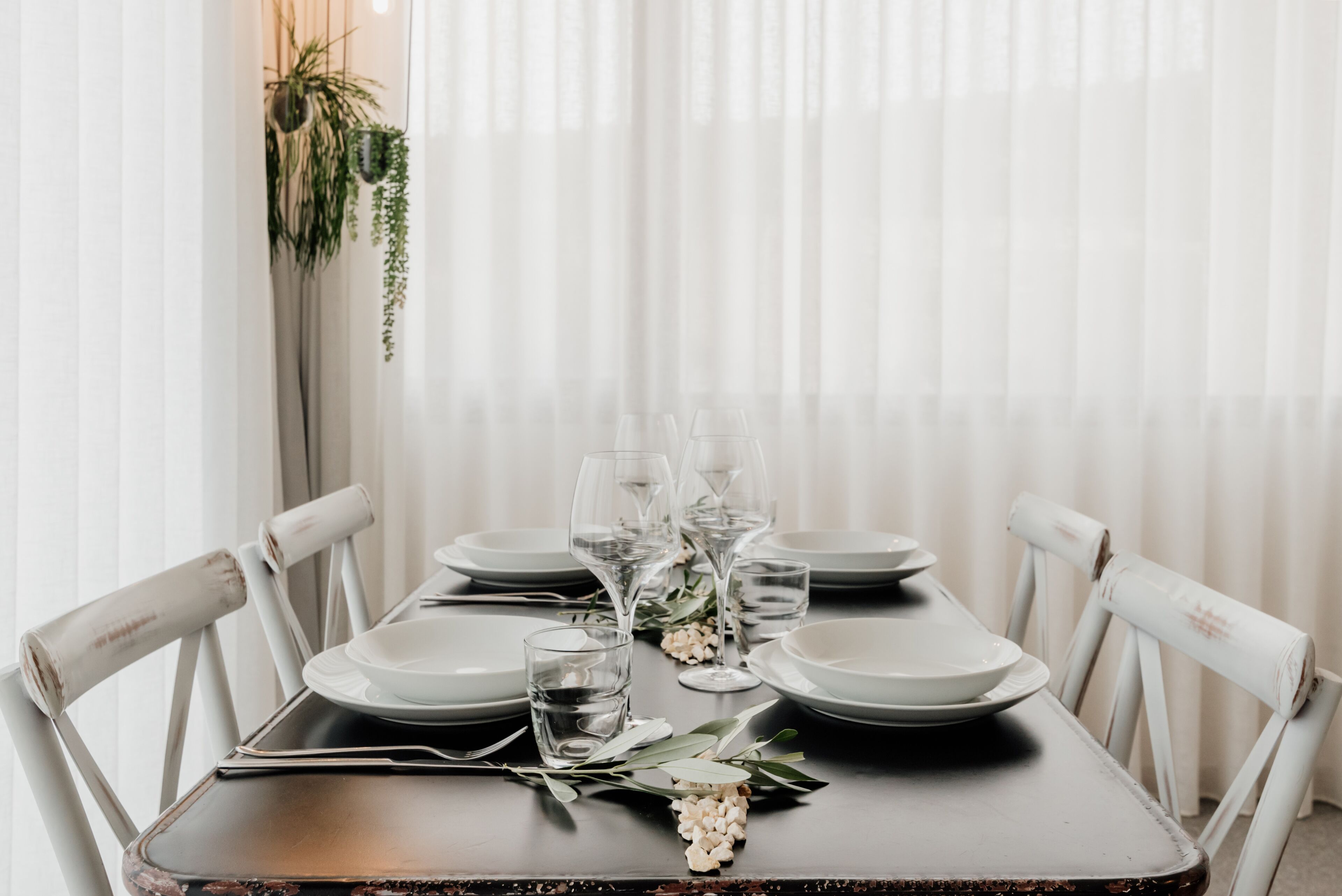 A dining table set with plates, glasses, and cutlery, surrounded by white chairs.