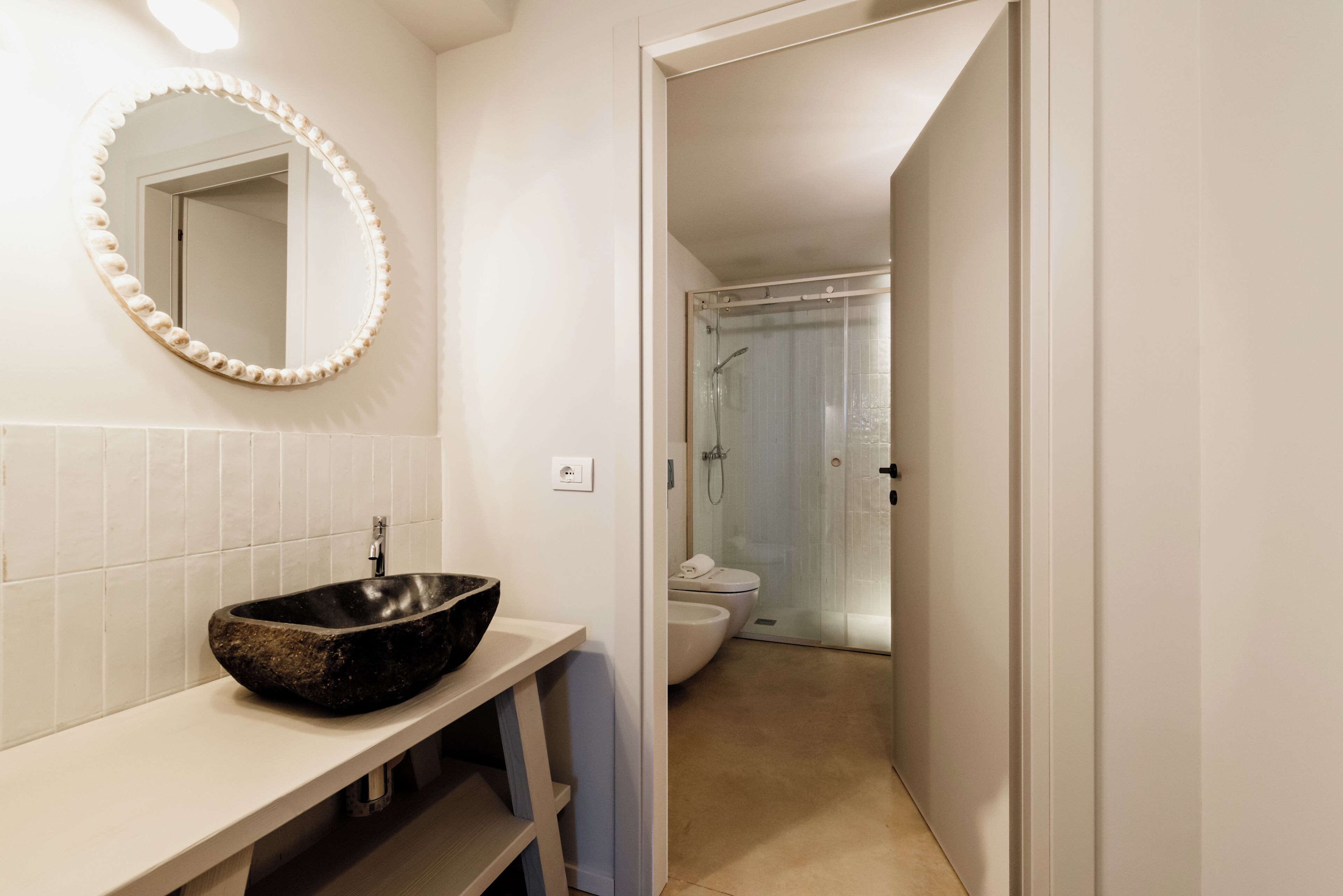 Un baño con lavabo de piedra, espejo con marco nacarado y zona de ducha con puerta de cristal.