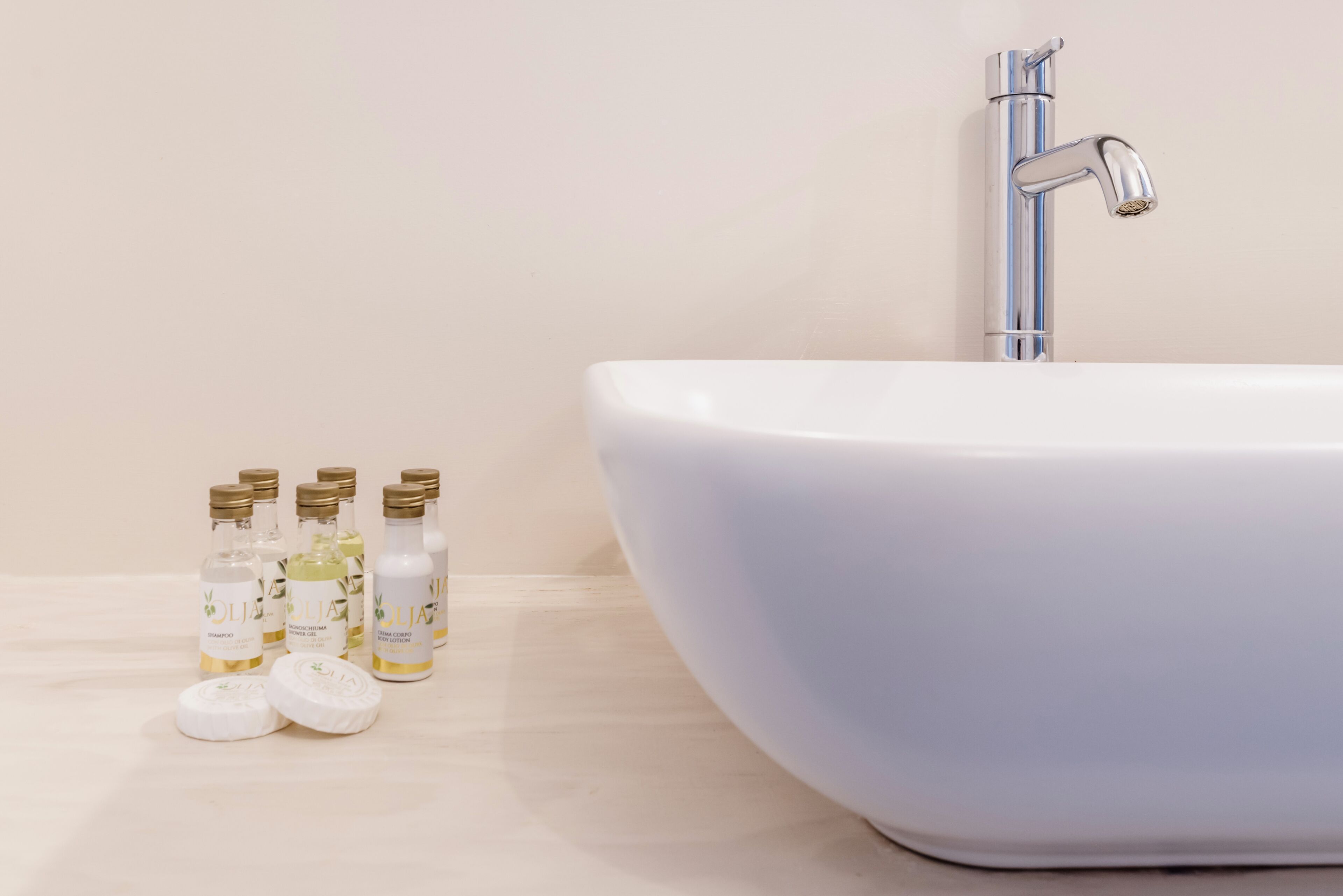 Ein Badezimmer mit einem weißen Waschbecken, einem Chrom-Wasserhahn und verschiedenen Shampoo- sowie Conditionierflaschen.