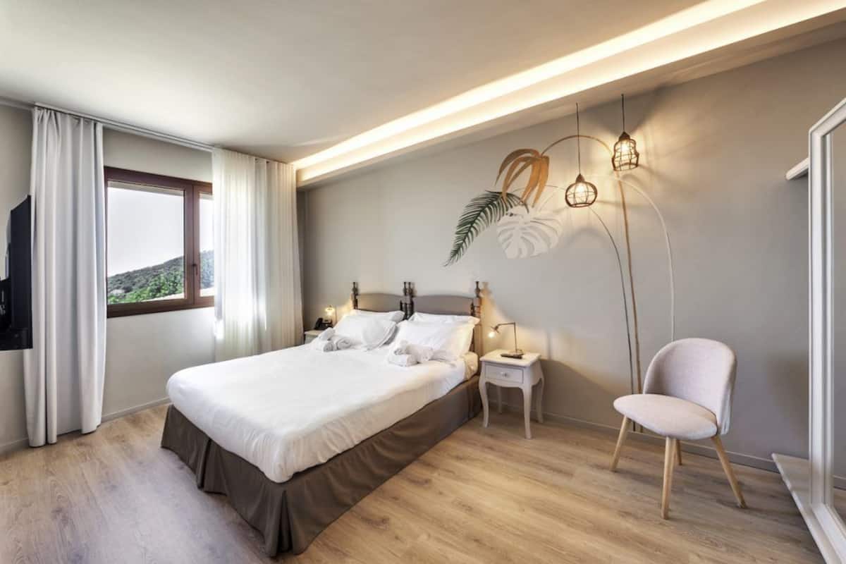 Una habitación de hotel moderna con una cama grande, mesitas de noche, una silla y una televisión.