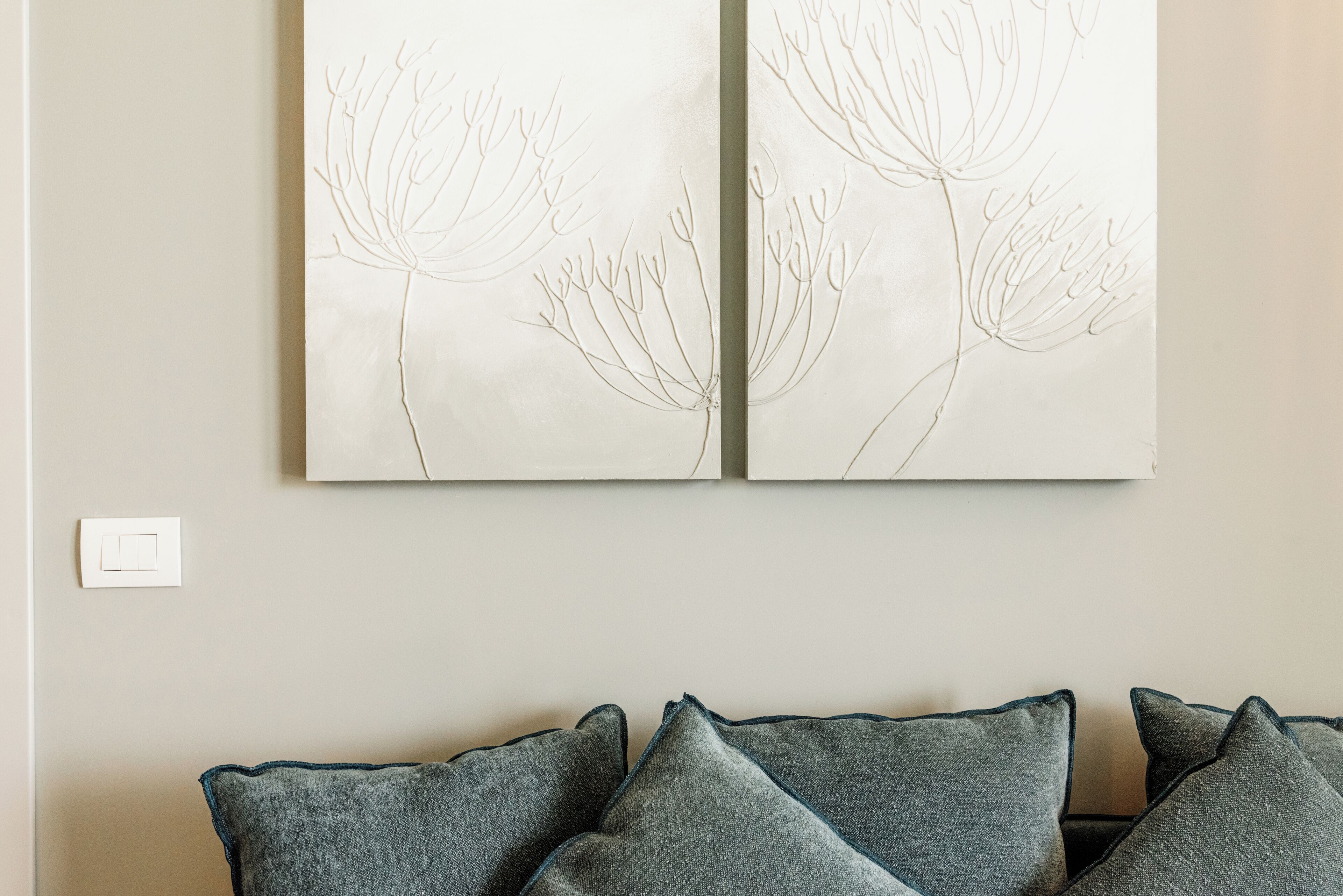 A wall with two framed botanical drawings and a grey couch with matching cushions.