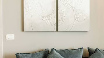 A wall with two framed botanical drawings and a grey couch with matching cushions.