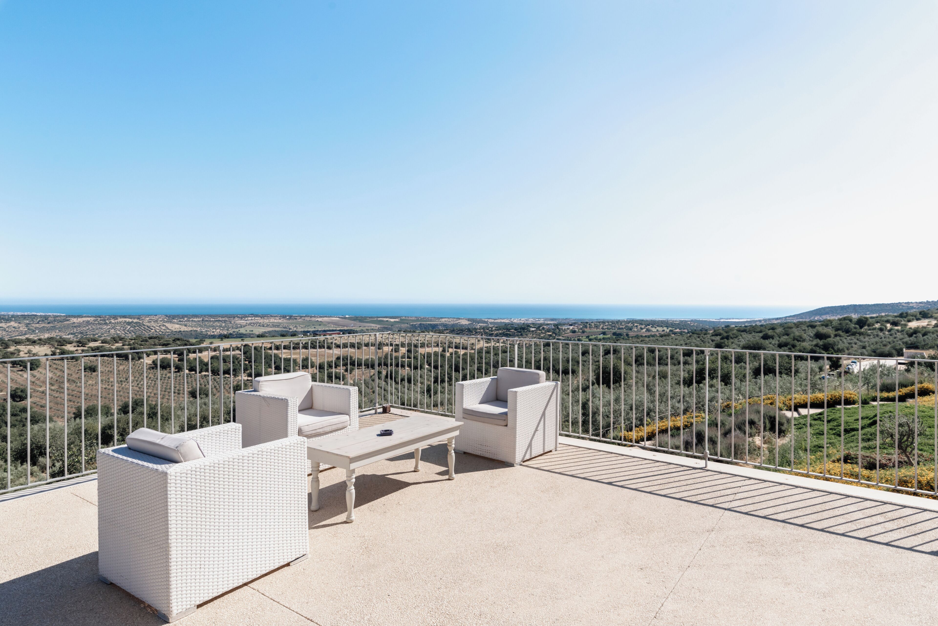 Una terrazza con mobili in vimini bianco, un tavolo e vista su un paesaggio lontano.