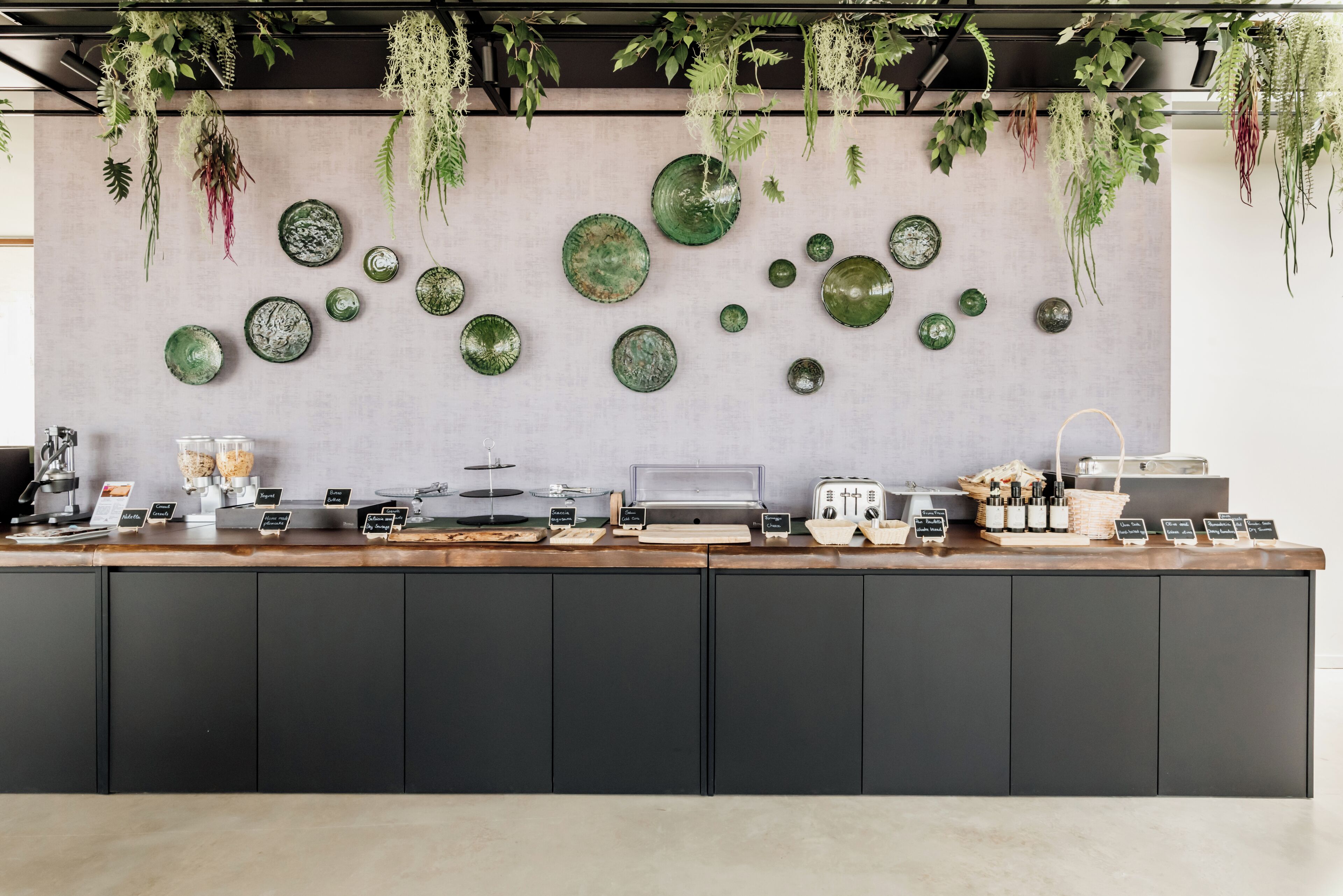 Un área de cocina moderna con encimera de madera, diversos electrodomésticos y platos decorativos verdes en la pared.