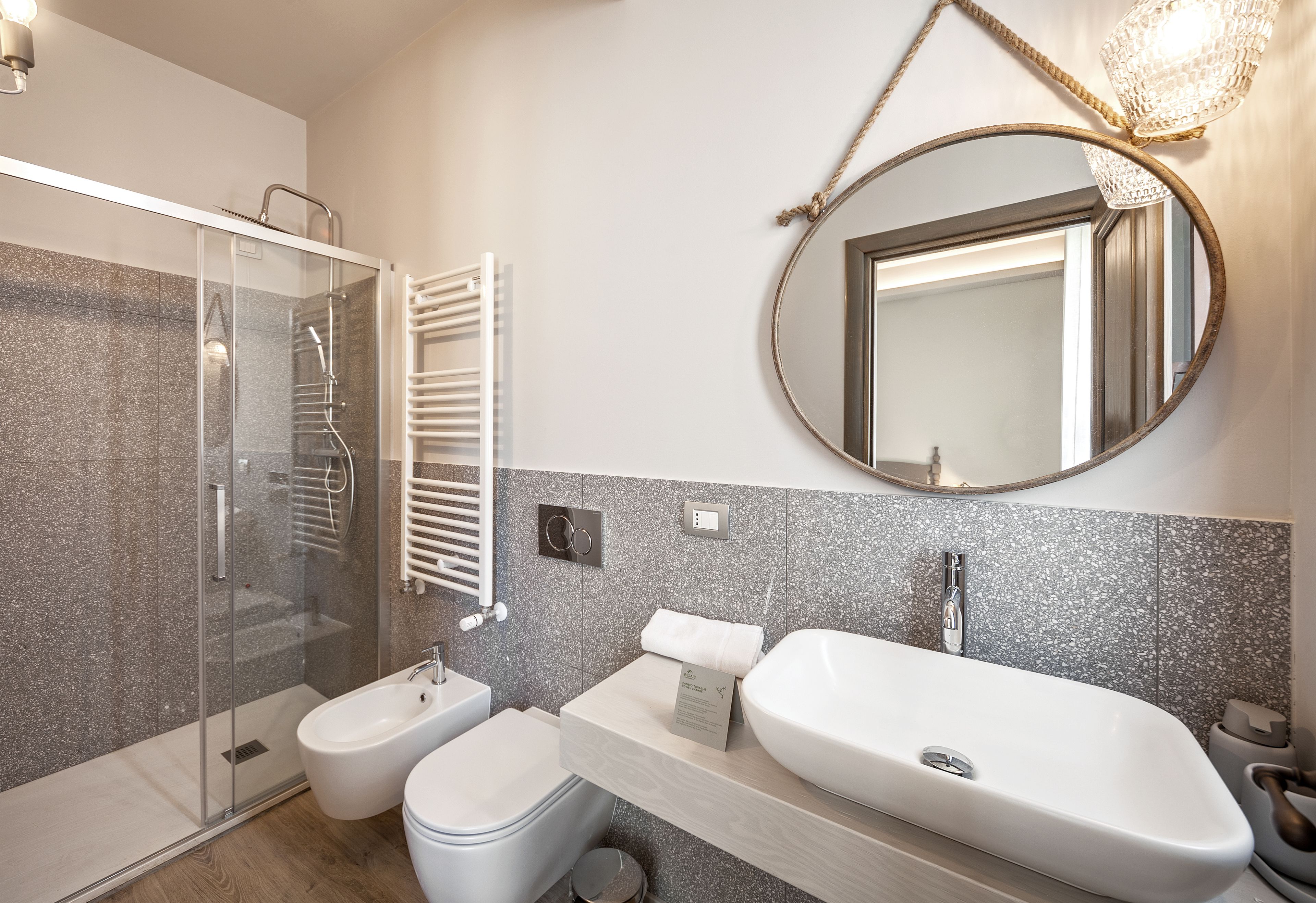 Une salle de bain moderne avec une douche à parois de verre, un bidet, un grand lavabo et un miroir rond.