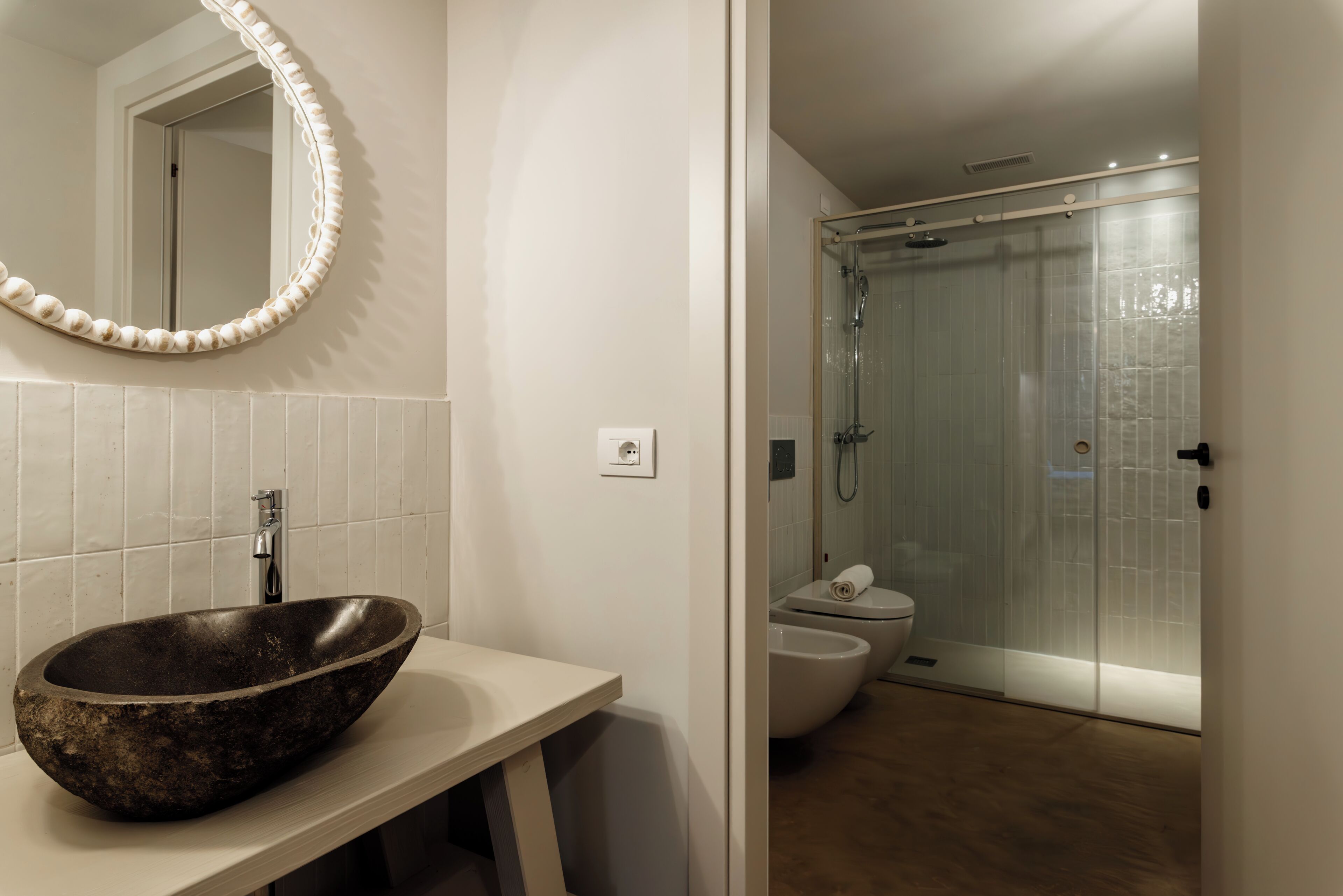 A bathroom with a stone sink, a mirror with a decorative frame, a toilet, and a glass-enclosed shower area.