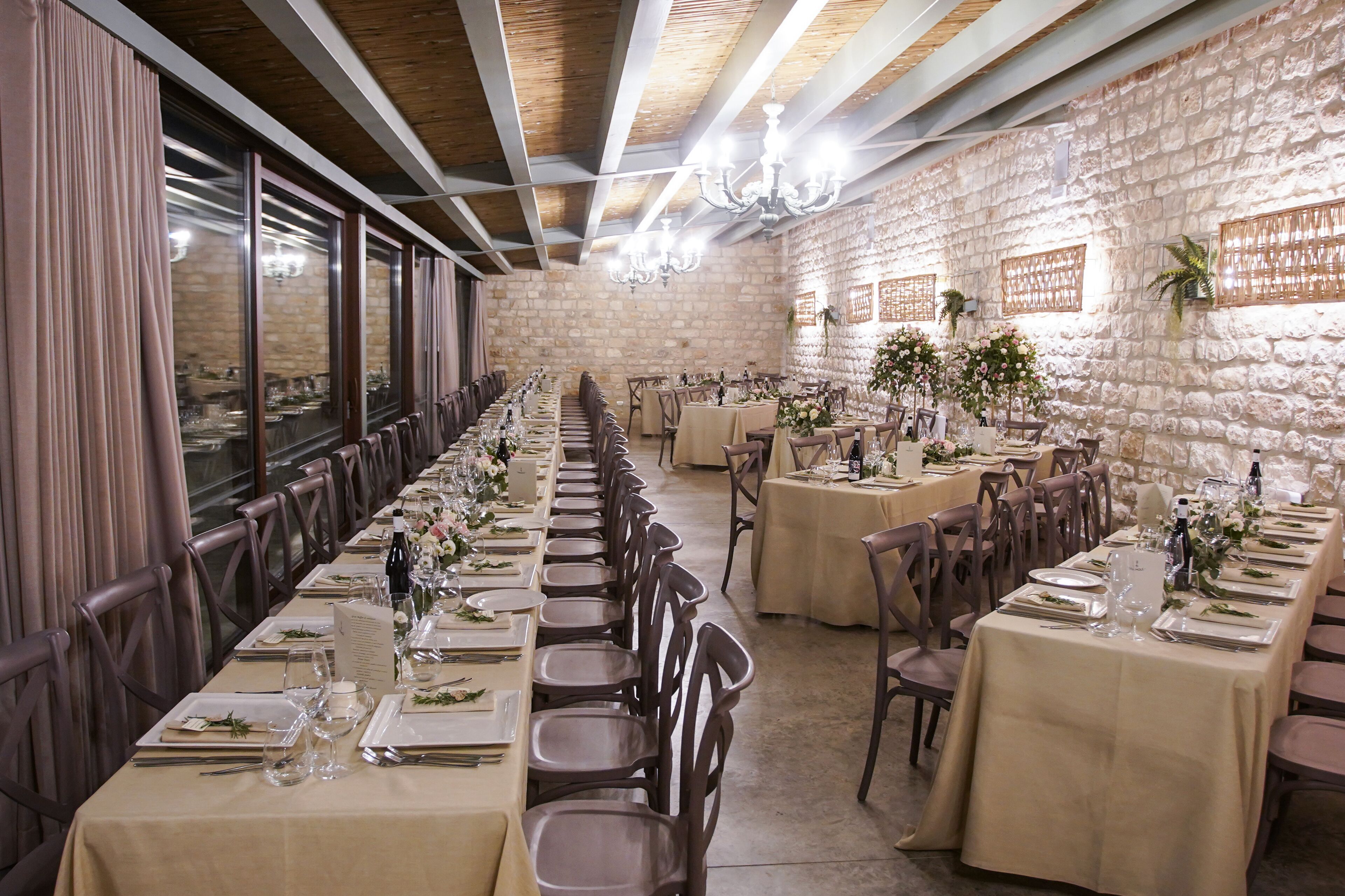 Una larga mesa de comedor dispuesta para un evento formal, con sillas a ambos lados, en una habitación con paredes de piedra y vigas de madera.