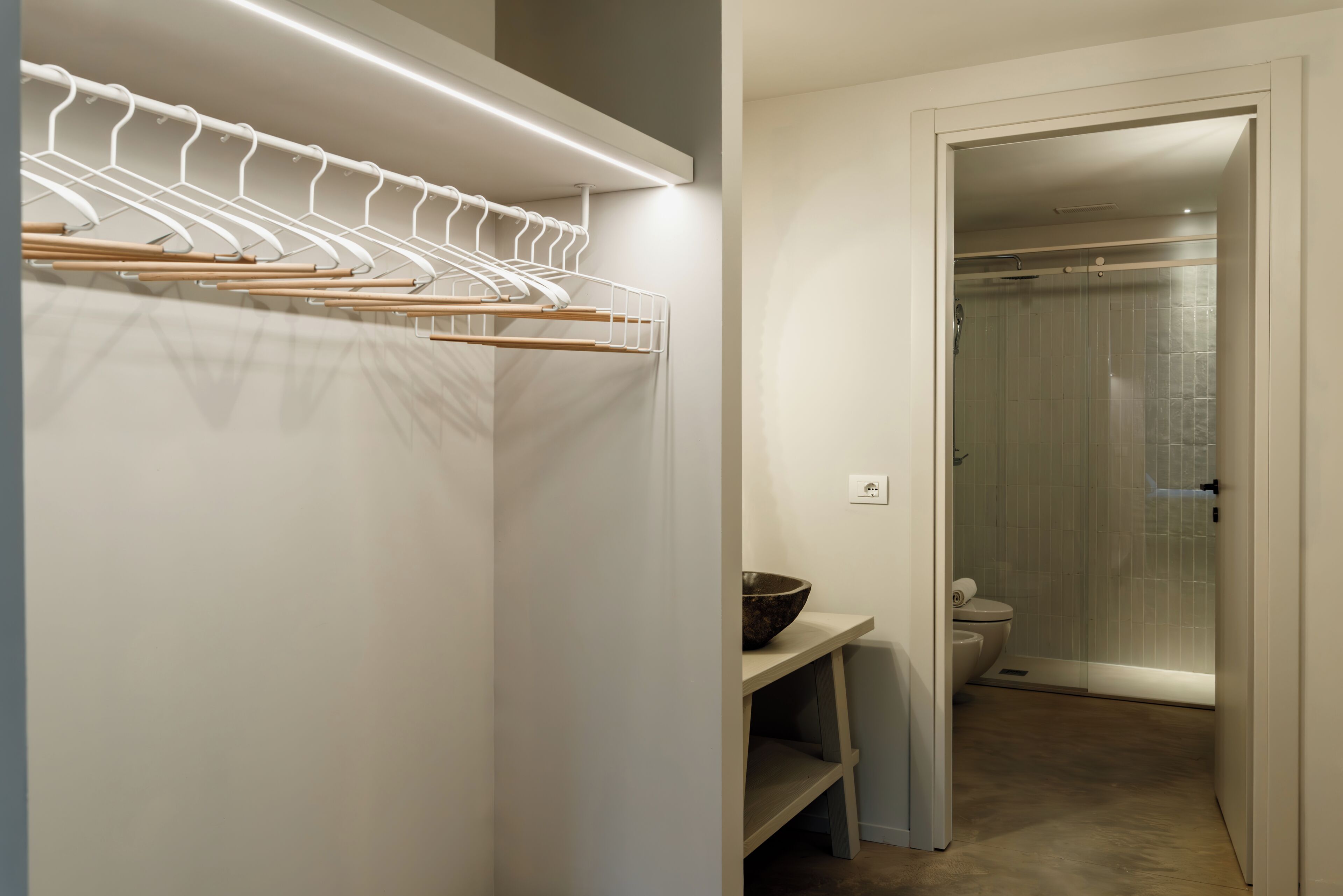 Un baño con ducha, inodoro y un perchero de madera con colgadores.
