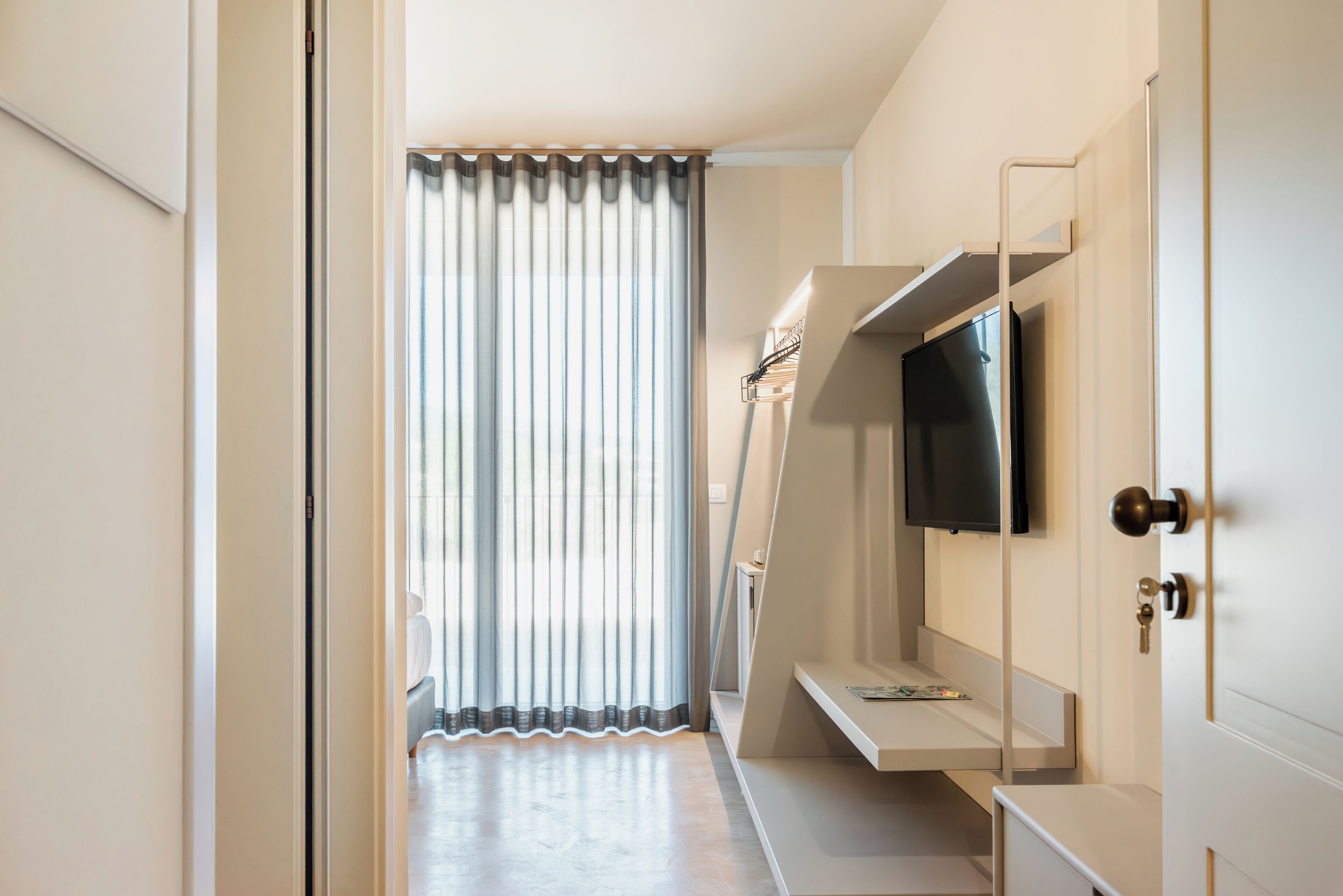 Une chambre d’hôtel moderne dotée d’une grande fenêtre, d’un téléviseur à écran plat fixé au mur et d’une banquette intégrée avec espace de rangement.