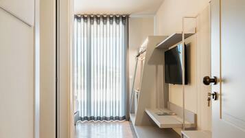 Una moderna camera d'hotel con una grande finestra, una TV a schermo piatto fissata al muro e una panca integrata con spazio contenitore.