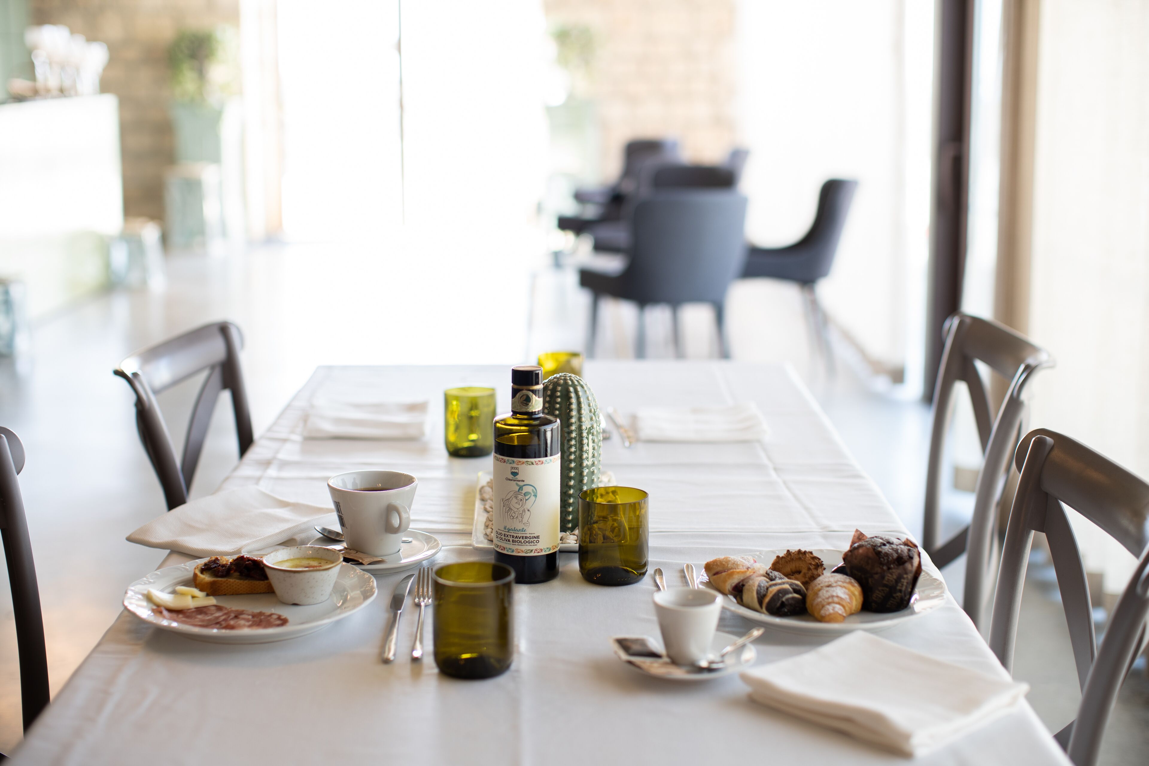 A dining table set with plates, cups, and a bottle, surrounded by chairs in a bright room with a view.