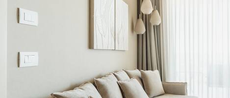 Quarto moderno com sofá bege, dois interruptores de luz na parede e uma janela grande com cortinas.
