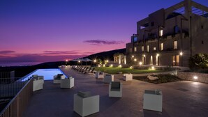 A modern building with a rooftop pool area, outdoor seating, and a view of the sea at dusk. - Relais Chiaramonte (Ragusa)