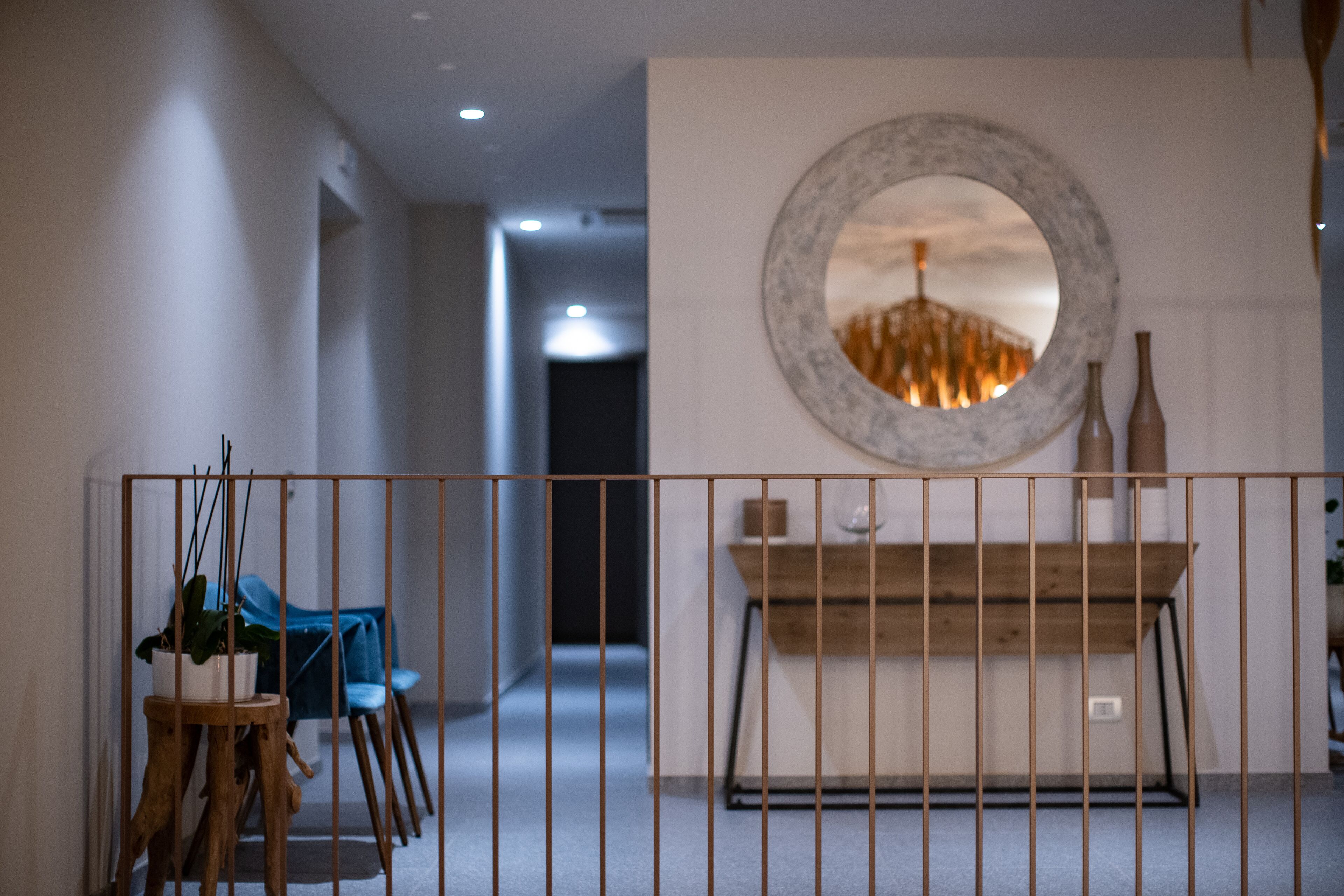 A hallway with a wooden bench, a round mirror, and a vase on a console table.
