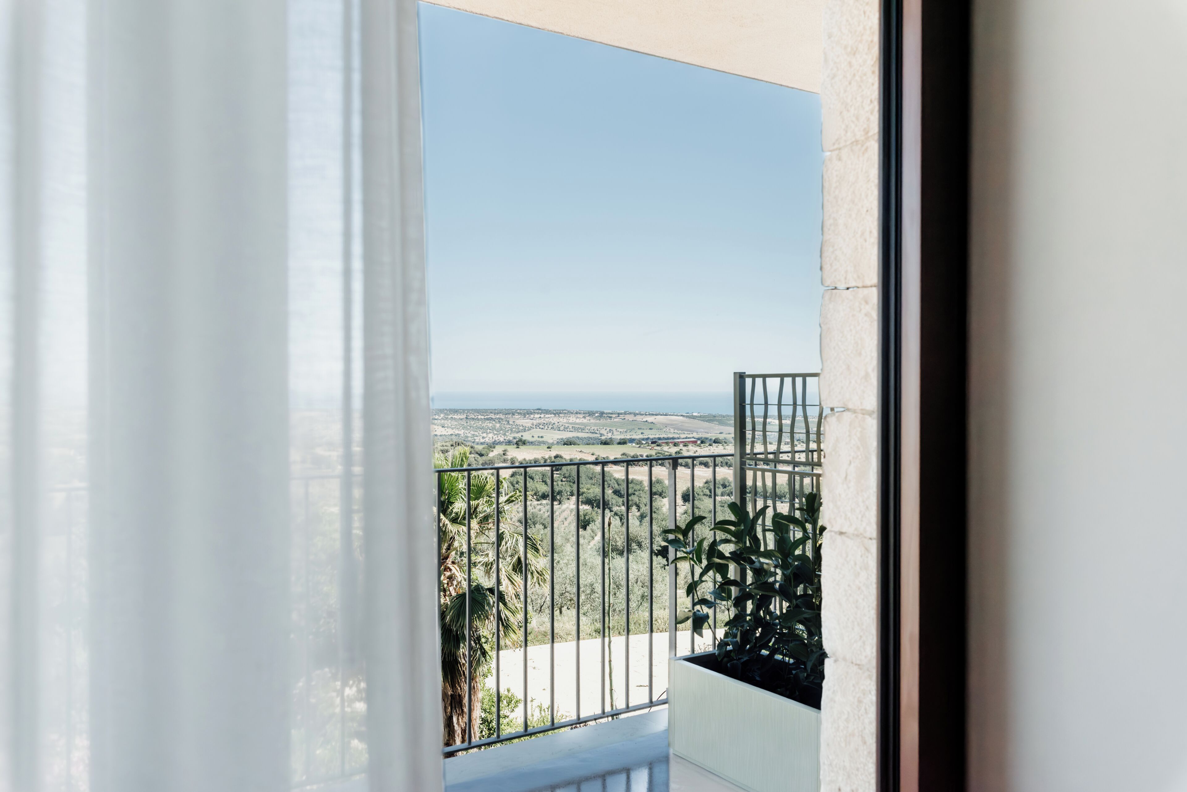 A balcony with a metal railing, a view of the sea, and a distant landscape.