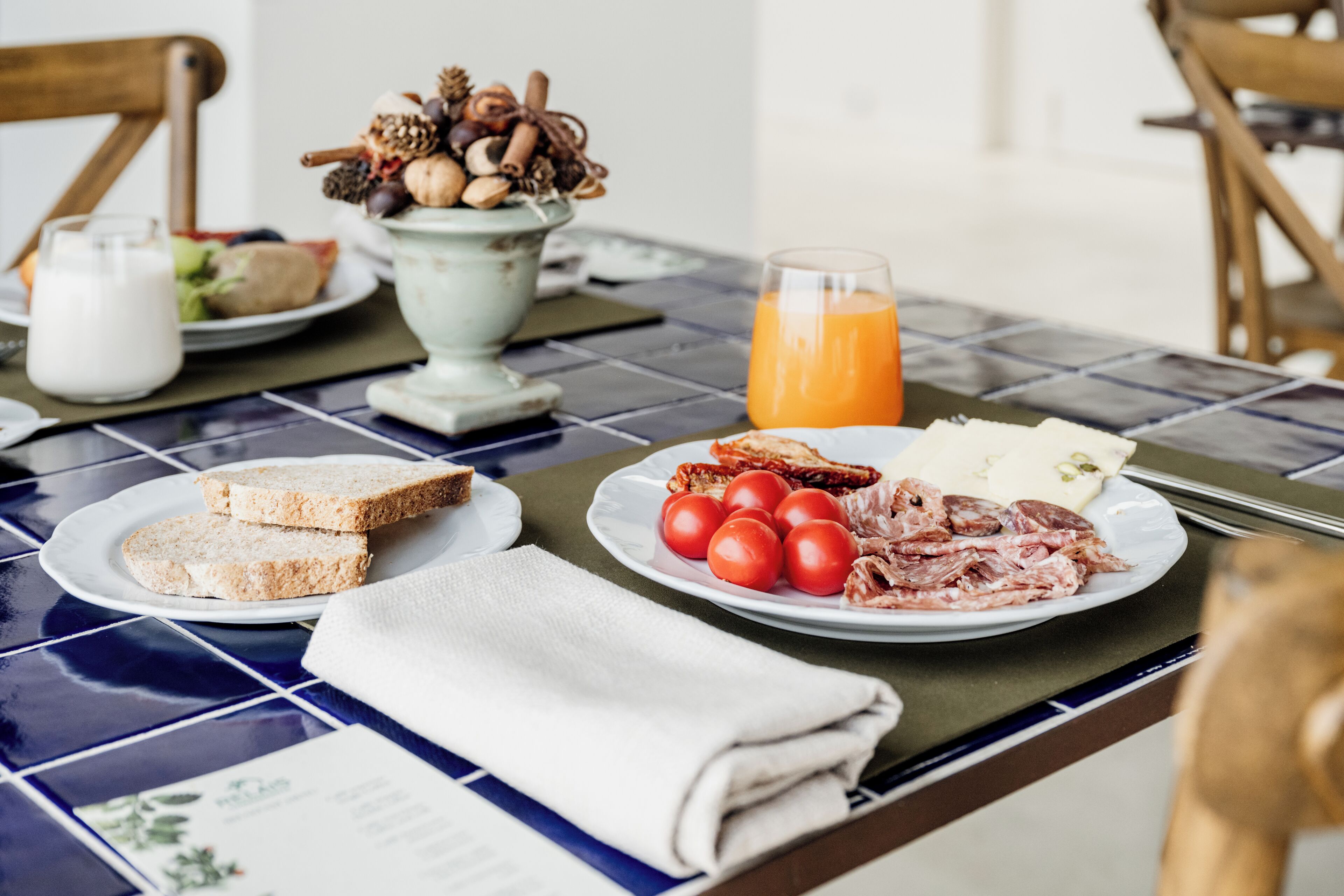 A breakfast table with plates of toast, tomatoes, cheese, and a glass of orange juice.