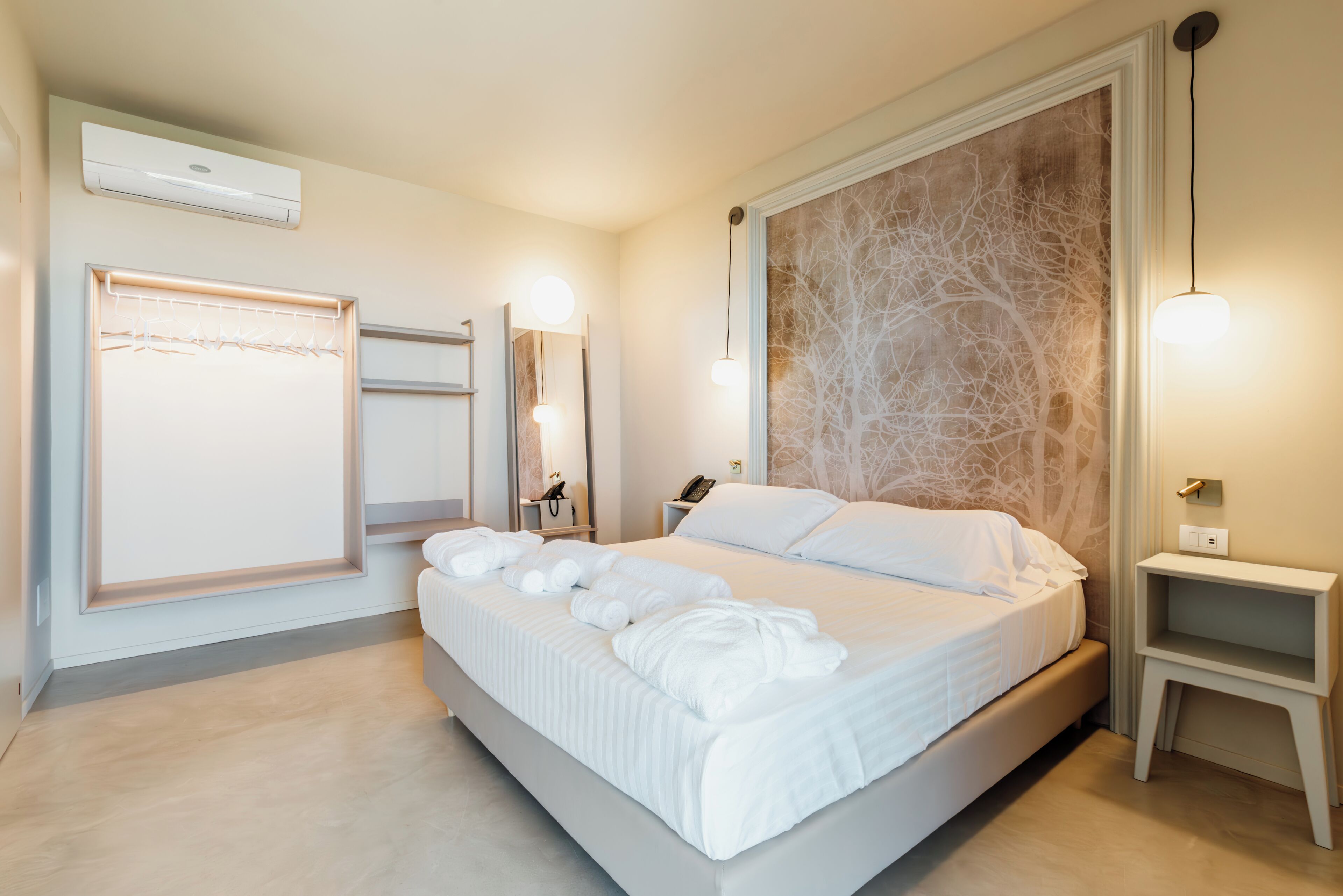 A modern bedroom with a large bed, a wardrobe, a mirror, a bedside table, and a wall-mounted air conditioner.