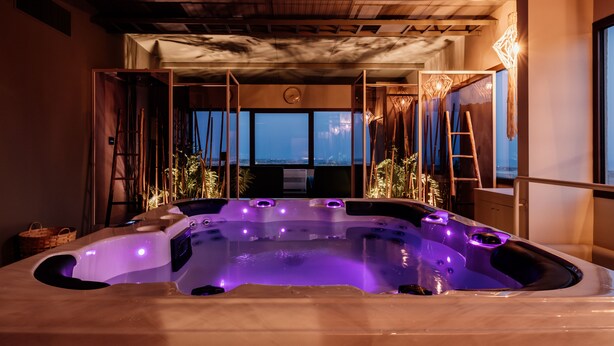 A hot tub with purple lighting, wooden ceiling beams, and a view of the ocean through large windows. - Relais Chiaramonte (Ragusa)