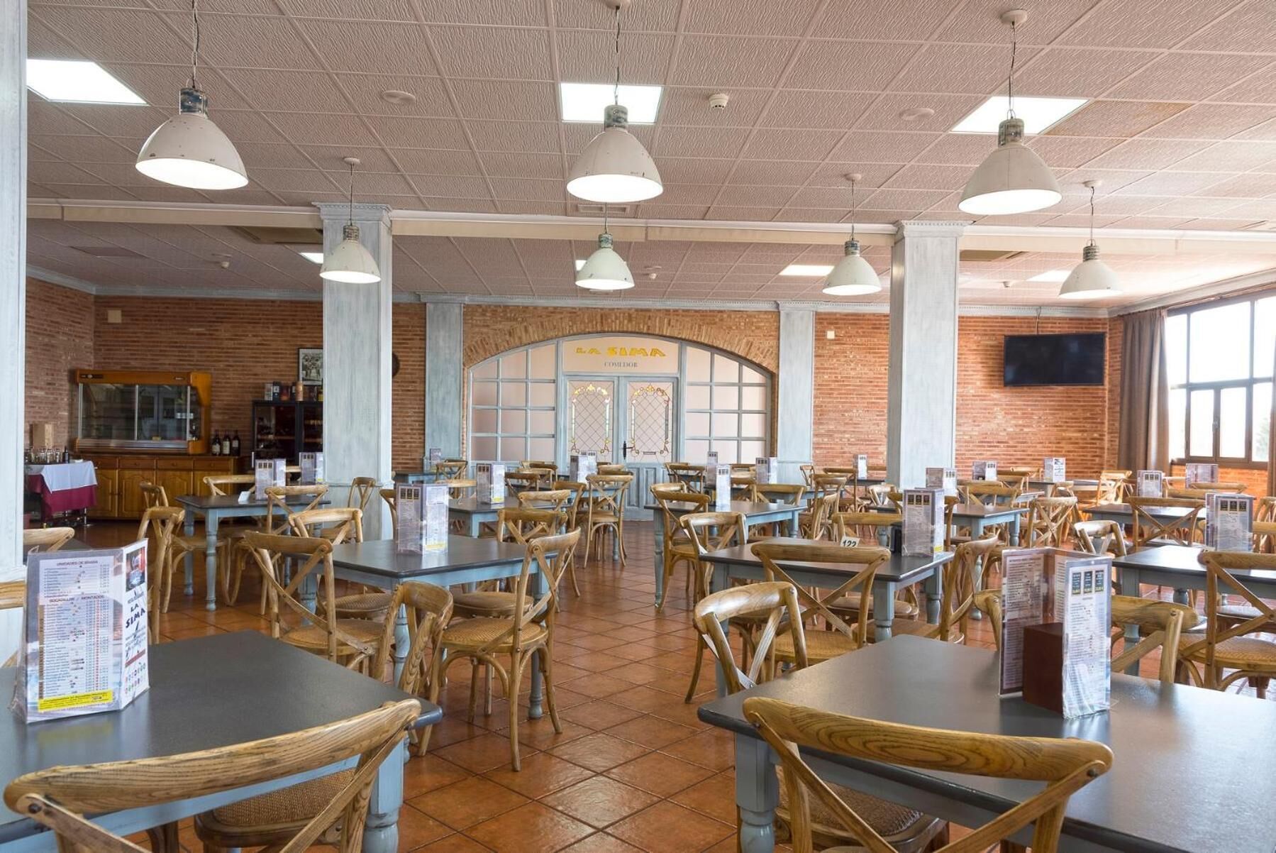 Una cafeteria àmplia amb diverses taules i cadires, una paret de maó i una finestra gran.