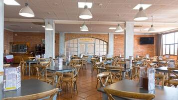 Una cafeteria àmplia amb diverses taules i cadires, una paret de maó i una finestra gran.