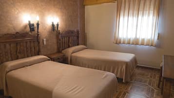 A room with two beds, a wooden headboard, a nightstand, a wall-mounted lamp, and a window with curtains.