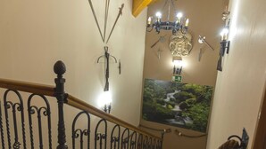 Un escalier orné de rampes en métal ouvragé, un lustre et des armes fixées au mur.