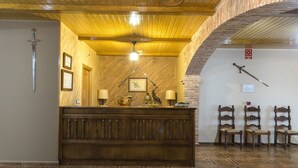 Un comptoir d’accueil en bois, des certificats encadrés et une épée accrochée au mur. Il y a trois chaises et un plafond en bois avec un luminaire.