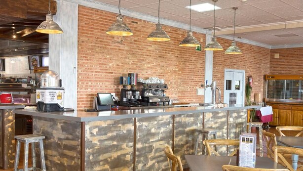 Un espace bar doté d’un comptoir en bois rustique, de luminaires suspendus et d’un mur en briques en arrière-plan.