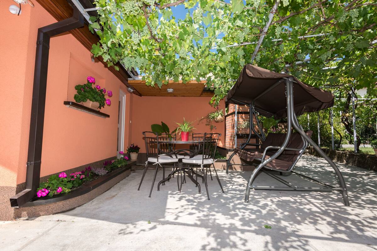 Une terrasse avec une table et des chaises, une plante suspendue et un fauteuil suspendu.