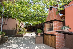 An outdoor patio area with a brick oven, potted plants, and a pergola with vines.