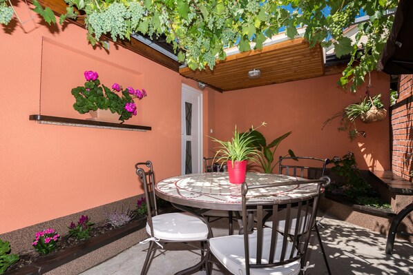 A patio with a round table and chairs, surrounded by potted plants and a wooden pergola.
