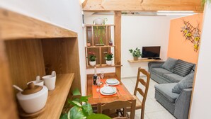 En kompakt opholdsstue med spiseplads, en grå sofa og et fjernsyn på en hylde.