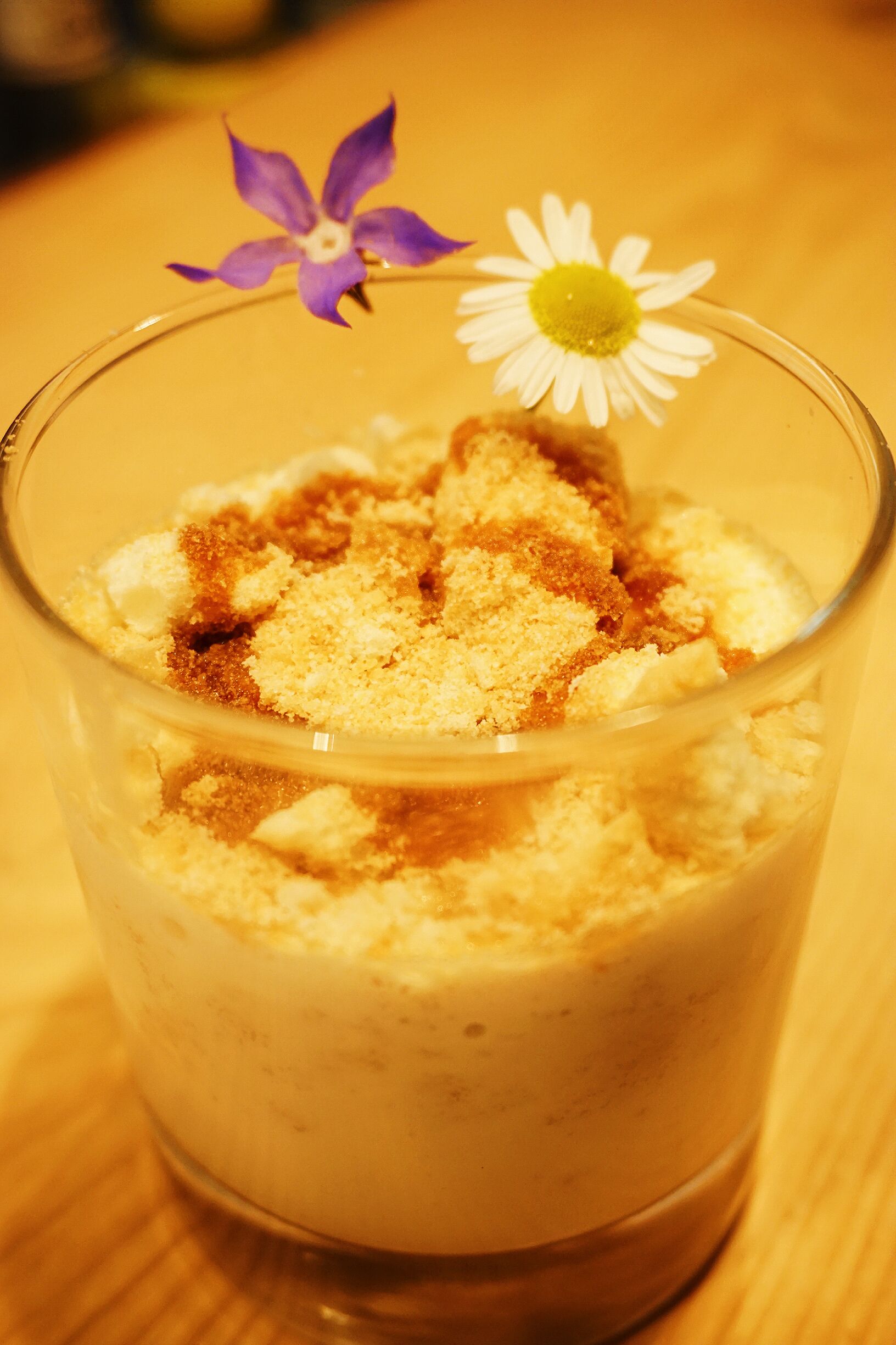 Un vaso con postre en capas, coronado con una flor y un toque de canela.