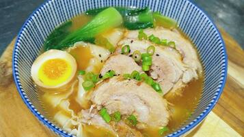 Un tazón de ramen con carne de cerdo en rodajas, un huevo cocido, cebolletas y bok choy en un tazón con borde azul.