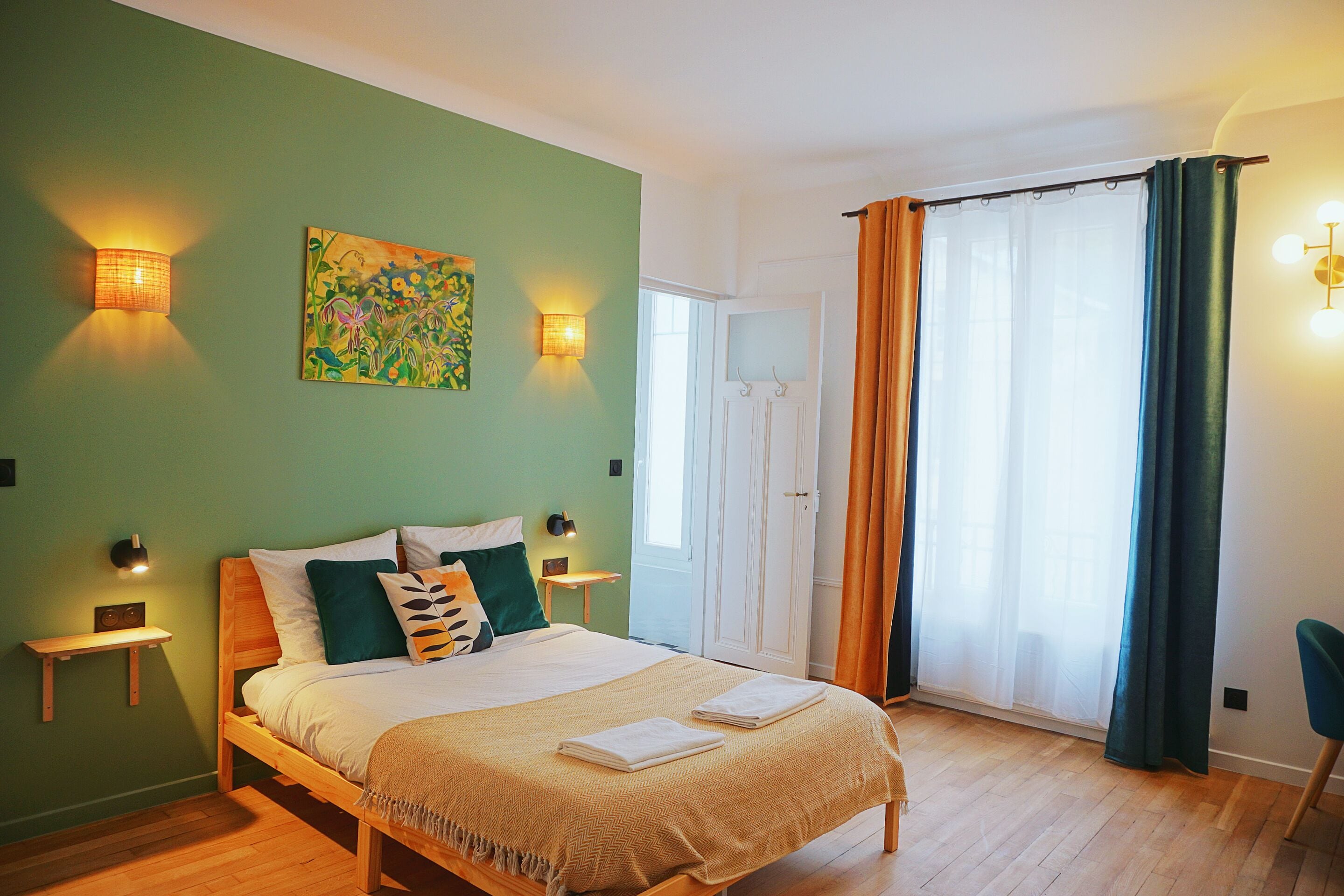 Un dormitorio con cama, mesitas de noche, un cuadro y una ventana con cortinas.