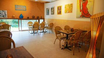 A restaurant interior with wicker chairs, a wooden table, and artwork on the walls.