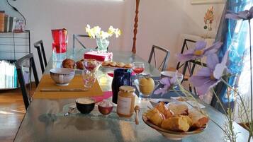A dining area with a glass table, chairs, a vase with flowers, and a painting on the wall.