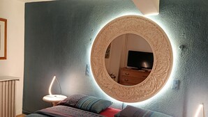 Un dormitorio moderno con un espejo redondo grande, dos mesitas de noche con lámparas, un edredón estampado y un aparador.