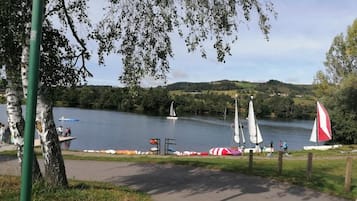 A lakeside park with a walking path, sailboats, and a sailboat rental area.