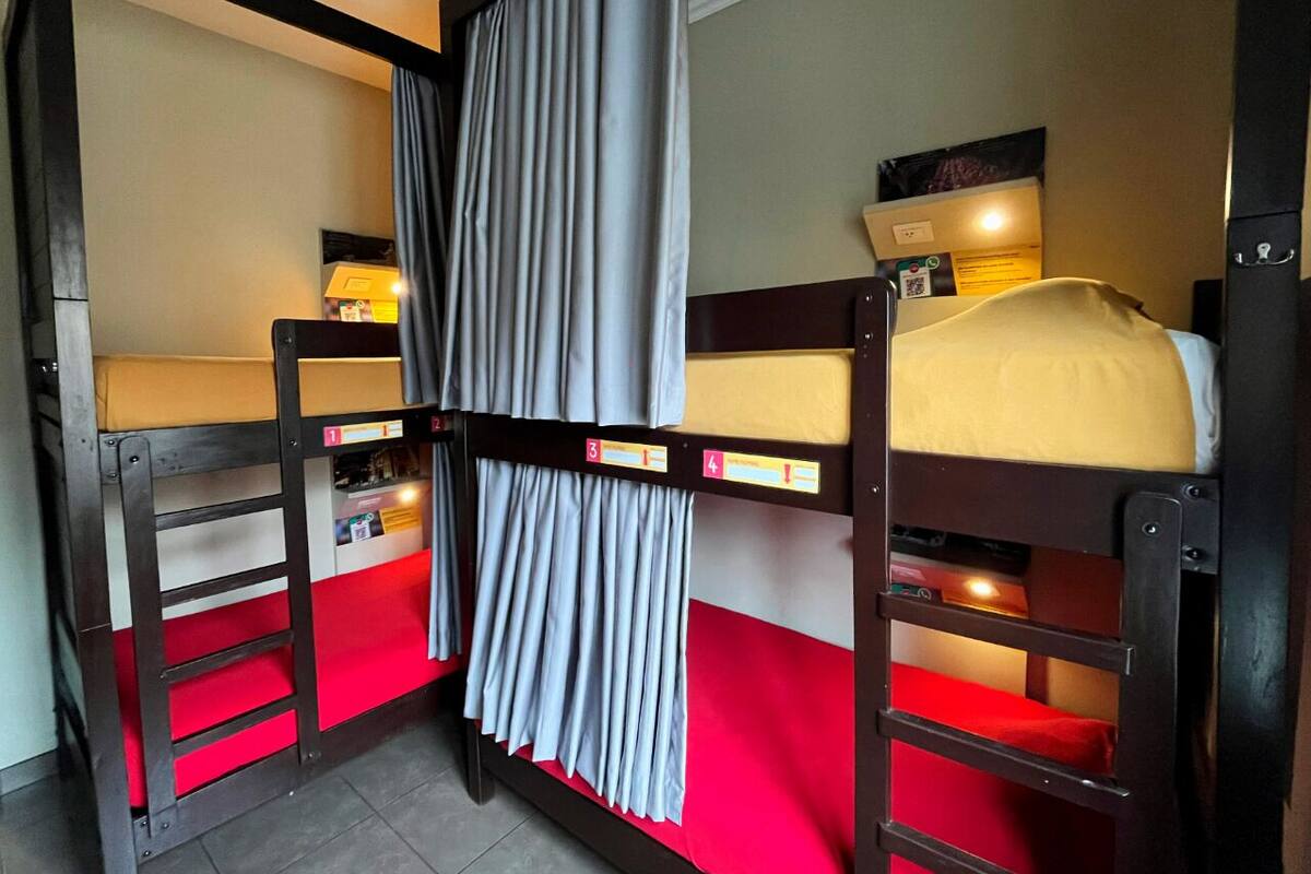 A bunk bed room with a red mattress, a curtain, and a small table with a lamp.