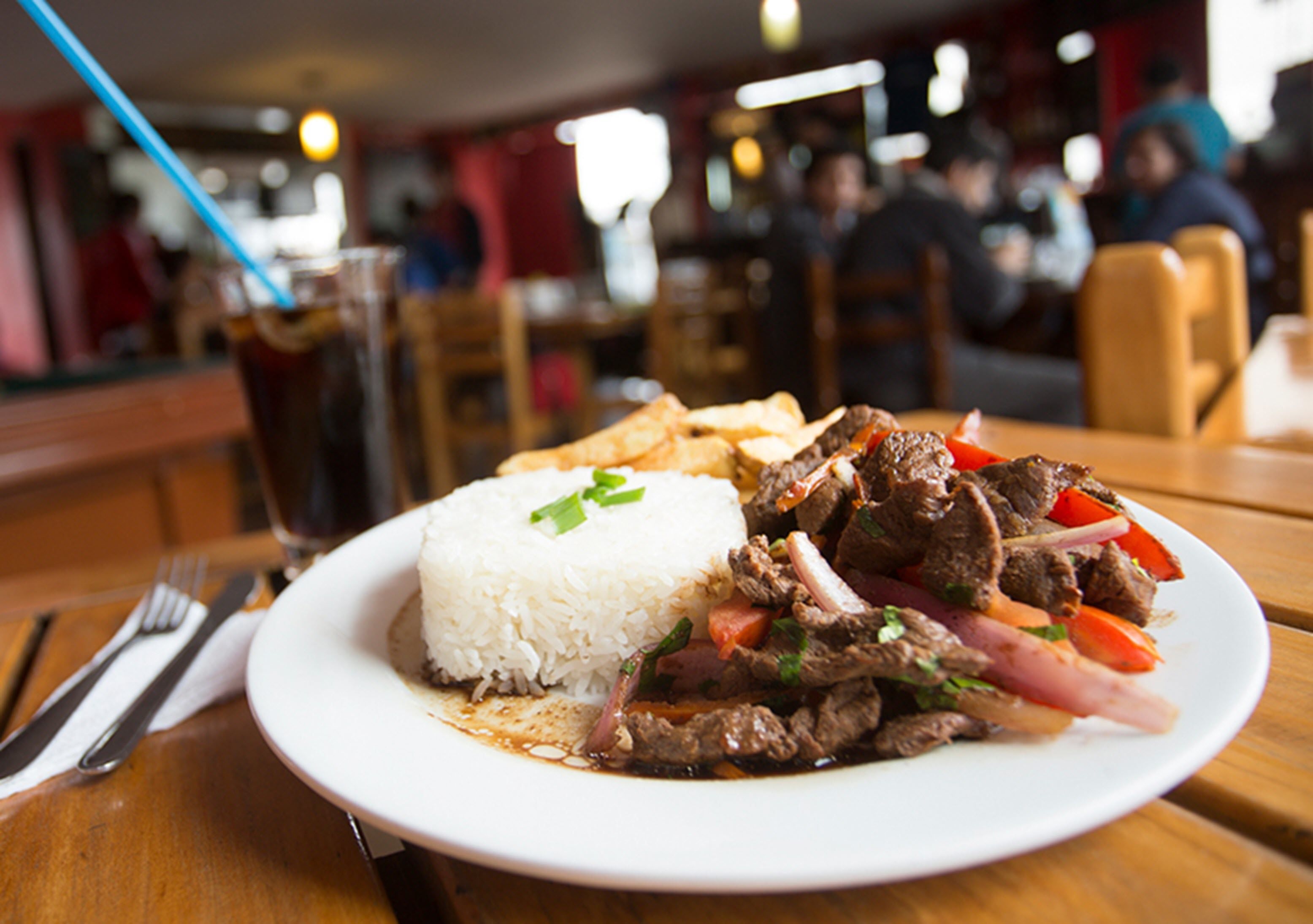 Un plato de carne con arroz y verduras sobre una mesa de madera en un restaurante.