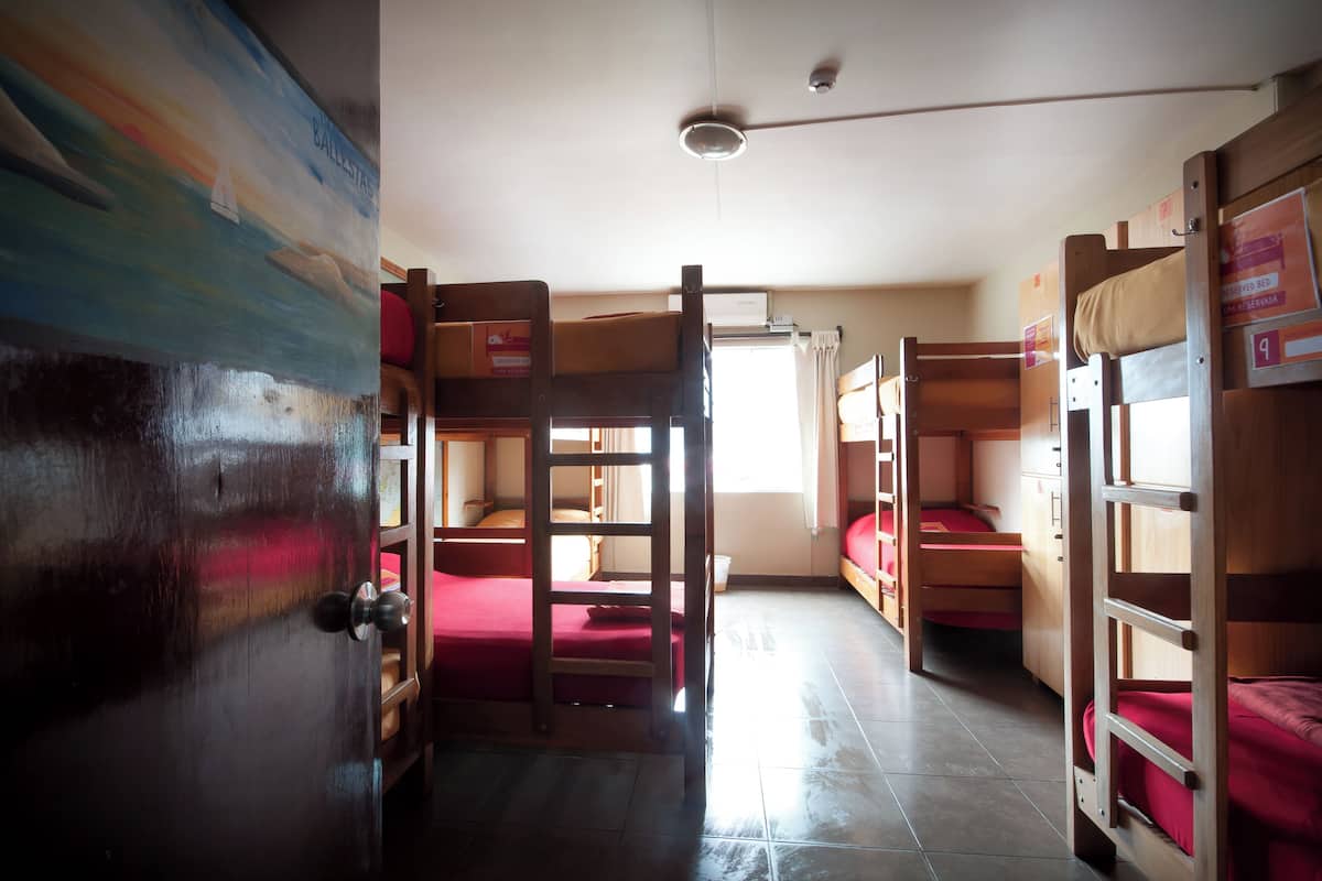 A dormitory room with bunk beds, a wooden door, and a ceiling fan.