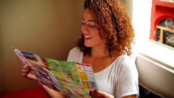 A person reading a colorful magazine by a window with a red wall in the background.