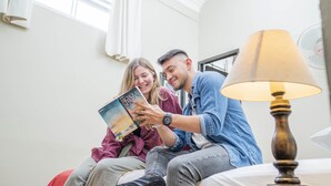 A couple sitting on a bed reading a book in a room with a lamp and a fan. - Pariwana Hostel Lima - Adults only (Lima)